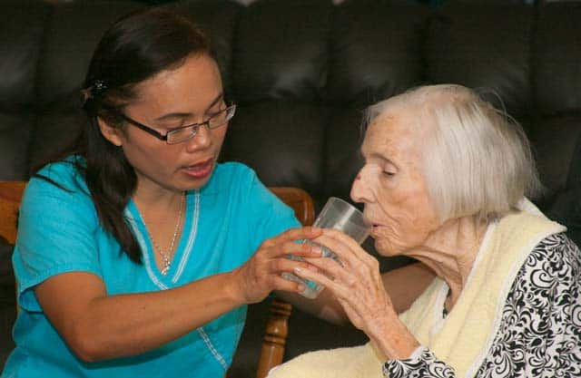 Caregiver providing services with helping drink fluids.